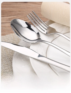 Polished stainless steel cutlery set with knife fork and spoon on white ceramic plate