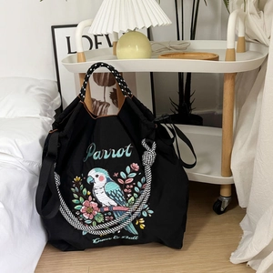 Close-up of black nylon tote bag featuring vibrant parrot and floral embroidery detailing