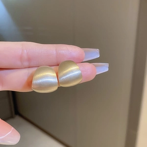 Detail of matte gold geometric curved stud earrings with brushed metallic finish
