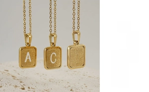 Primer plano de tres collares dorados con letras caladas A, C y R sobre fondo mate