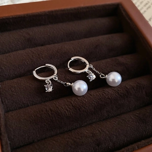 Detailed close-up of zircon and pearl tassel hoop earrings on velvet display