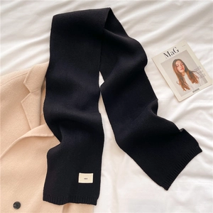 Close-up of thick black knit scarf with emo woven label on soft white fabric background