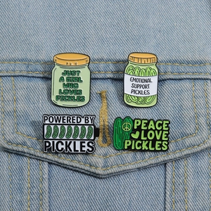 Detailed view of four cartoon pickle enamel pins pinned on a blue denim jacket pocket