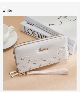 Detailed view of white embossed long wallet with double zippers and wrist strap on a desk