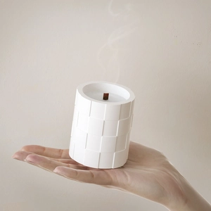 White cylinder candle with textured mosaic pattern and wood wick held in hand