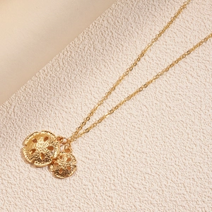 Detail der Goldkette mit strukturierten runden Doppelanhängern auf beigem Grund
