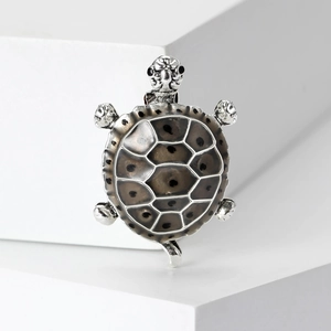 Macro detail of silver turtle brooch with grey translucent shell on a clean white pedestal