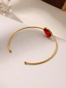 Detailed view of an open gold bangle featuring a large faceted deep red gemstone