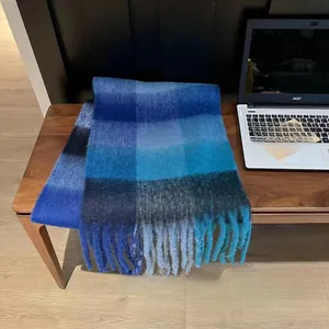 Detail of blue and black plaid scarf with long tassels on a wooden surface