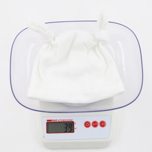 Bonnet en tricot côtelé blanc pour bébé pesé sur une balance électronique affichant 39g