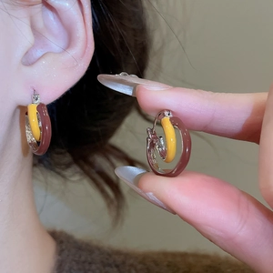 Detail of vintage double hoop enamel earrings in yellow and brown worn on ear
