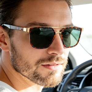 Close-up of tortoise shell sunglasses with gold frames worn by a male driver in a car