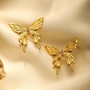 Macro shot of gold butterfly earrings with pink crystal on beige silk fabric