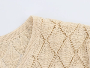 Detailed close-up of beige knitted cardigan showing hollow diamond pattern and ribbed V-neck