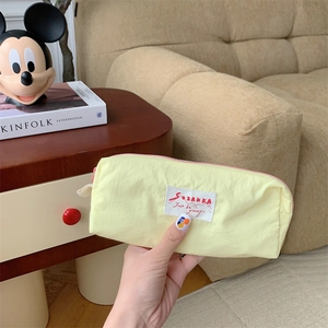 Close-up of yellow fabric pouch with pink zipper and side handle held by hand