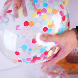 Transparent party balloon with colorful confetti dots being held by hand for decoration