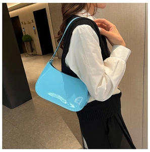 Close-up of a glossy light blue patent leather baguette bag styled as an underarm shoulder bag