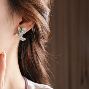 Detail view of silver bow-shaped tassel earring with green stones on a model