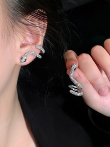 Détail macro d'une boucle d'oreille serpent argentée avec œil en pierre verte et zircon
