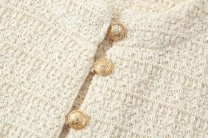 Détail macro de la texture du cardigan en maille crème avec boutons dorés gaufrés