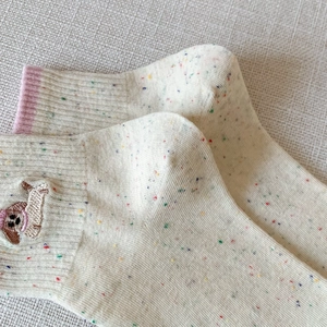 Detailed embroidery of a dachshund on cream cotton socks with colorful speckled yarn