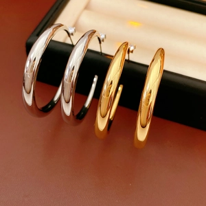 Macro shot of silver and gold C-shaped hoop earrings on beige velvet jewelry tray