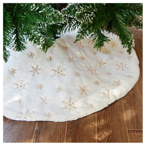 Detail of plush white Christmas tree skirt with golden snowflake embroidery on wood floor