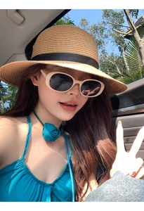 Detail of a brown woven straw sun hat styled with retro cream sunglasses in a car