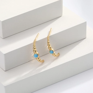 Macro shot of gold beaded stud earrings featuring a blue round opal stone on white blocks