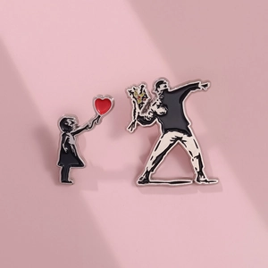 Detail of two metal enamel pins featuring street art heart balloon girl and flower thrower
