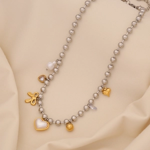 Detail of beaded necklace with golden bow, heart pearl, and zircon pendants on silver chain