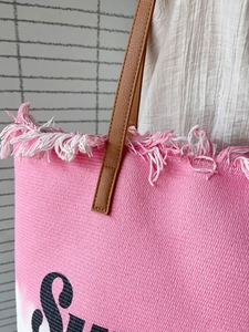 Detail der rosa geflochtenen Tragetasche mit Fransenbesatz und braunen Lederriemen