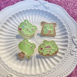 Set de cuatro lindos pins de esmalte de rana con formas de comida y macarons