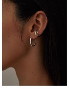 Close-up of a silver double-layered ear cuff and oval hoop earrings on a female model