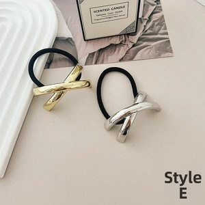 Detail of gold and silver metallic X-shaped elastic hair ties on a minimalist tray