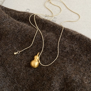 Dettaglio macro del ciondolo a forma di zucca hulu in oro spazzolato su catena snake