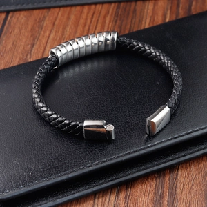 Detail of black braided leather bracelet with silver magnetic buckle on wooden table