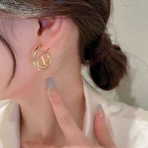 Close-up of a model wearing golden heart earrings with hollow letter cutouts