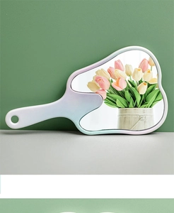 Detail of cute tooth-shaped hand mirror with white handle and gradient pink frame on a desk