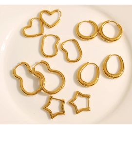 Flat lay of multiple gold geometric earrings including heart and star shapes in a white dish