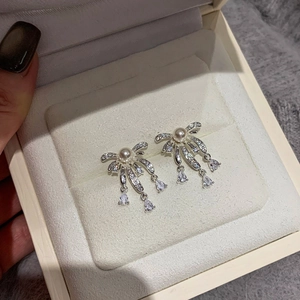 Elegant silver bow earrings with hanging pearl and zircon drops in a jewelry gift box