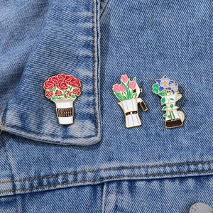 Three enamel pins featuring coffee cups and flowers pinned on a blue denim jacket