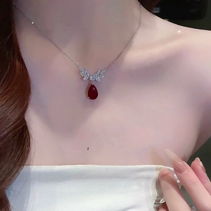 Macro detail of teardrop ruby pendant with silver angel wings on a woman's collarbone