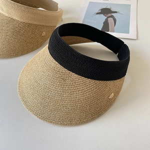 Detail of straw sun visor featuring fine weave texture and elastic band with metal leaf logo