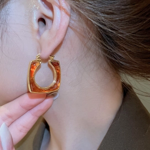 Close-up of amber resin U-shaped earrings with 18k gold plating on a female model