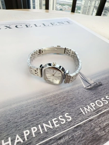 Detail of silver square quartz watch with steel link strap on a magazine background