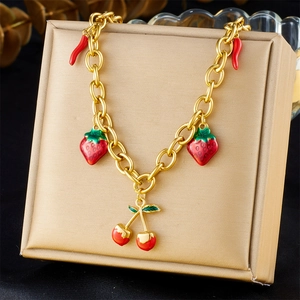 Detailed close-up of gold chain necklace with red enamel strawberry and cherry pendants