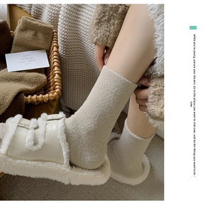Close-up of thick knitted thermal socks in oat white with fuzzy slippers and home decor