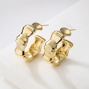 Polished gold plated C-shaped bamboo hoop earrings on a white marble surface