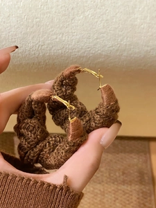 Detailed view of large brown knitted hoop earrings with twisted wool texture and gold clasps